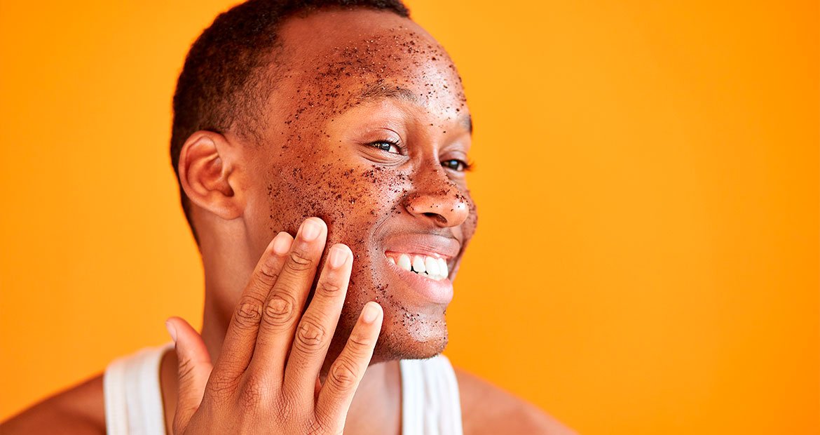 Homem negro sorri ao esfoliar o rosto com esfoliante físico